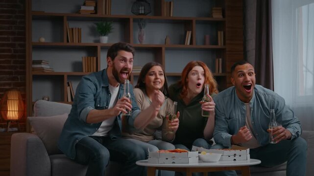 Overjoyed four multiracial friends watching football fans excited win watch tv television successful sport team triumph achieve diverse women men on home party enjoying soccer clinking bottles cheers