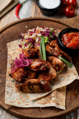 Grilled chicken wings are arranged on a wooden platter, complemented by a vibrant salad and a small bowl of spicy sauce. The warm tones of the setting enhance the appetizing look