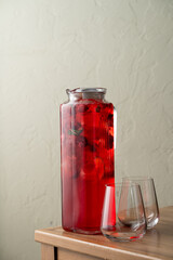 A vibrant pitcher filled with a berry-infused drink rests on a wooden table. Two glasses await nearby, ready for a refreshing sip on a warm day