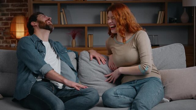Happy family couple at home talking wife woman telling funny story joke man laughing amazed husband having fun listening humorous joke man boyfriend with girlfriend on couch laugh married partners