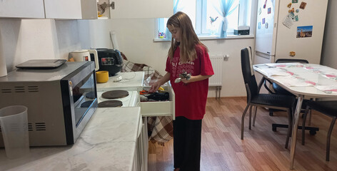 A girl cooks in a modern kitchen with a cutlery drawer open