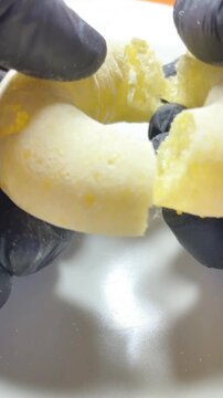 Hands wearing black gloves breaking a doughnut in close-up on a white tray - Vertical video