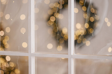 White wooden window frame with glass in an indoor festive setting, showing blurred warm lights and a wreath detail. Suitable for holiday themes, decoration concepts, celebration visuals.