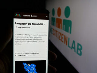 Fototapeta premium Stuttgart, Germany - 11-19-2025: Person holding smartphone with web page of Canadian research laboratory Citizen Lab on screen in front of logo. Focus on center of phone display.