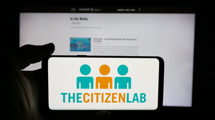 Fototapeta premium Stuttgart, Germany - 11-19-2025: Person holding cellphone with logo of Canadian research laboratory Citizen Lab on screen in front of webpage. Focus on phone display.