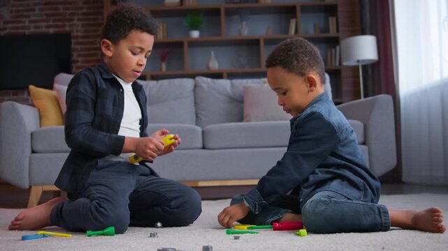 Two cute African American children playing with toys on floor at home enjoying entertainment concentrated kids little friends siblings brothers boys play game happy family weekend hobby together joy