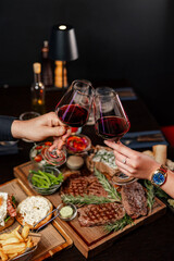 Clinking red wine glasses over a gourmet steak dinner
Elegant dinner scene with red wine and grilled steaks
Celebratory wine toast above a rich meat platter