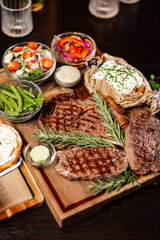Grilled steak assortment served with fresh sides and herbs
Beef steaks on wooden boards with vegetables and sauces
Steak platter featuring ribeye and rustic garnishes