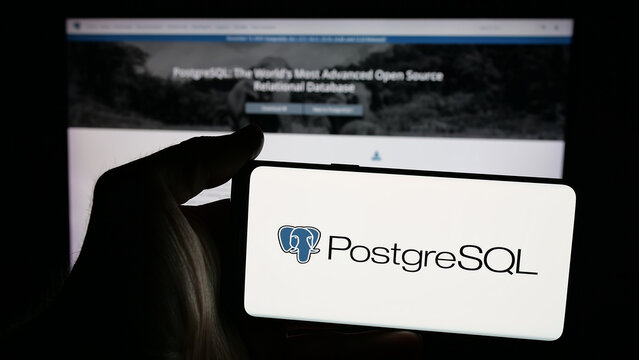 Stuttgart, Germany - 11-19-2025: Person holding mobile phone with logo of database management system PostgreSQL on screen in front of web page. Focus on phone display.