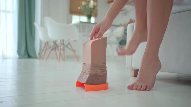 A compression stocking is stretched over an assist device on the floor as a senior woman prepares to put it on.
