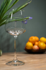 Elegant wine glass stands on wooden table, surrounded by fresh fruits in a bowl, with green plants in the background, showcasing a vibrant dining atmosphere