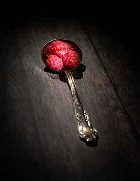 Framboises dans une cuill&egrave;re sur planche bois, int&eacute;rieur sombre,  verticale