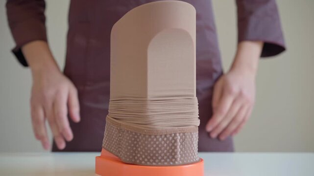 A woman positions a compression stocking on an assist device, showing her hands and the smooth elastic fabric prepared for supportive medical use.