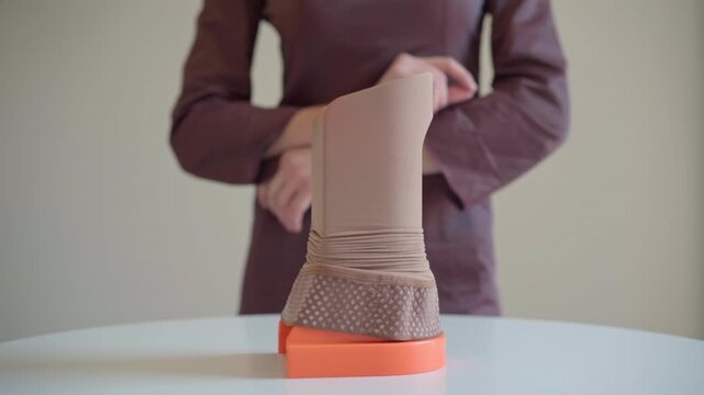 A compression stocking is stretched over an assist device that rotates on a turntable, showing the fabric and setup prepared for supportive medical use.