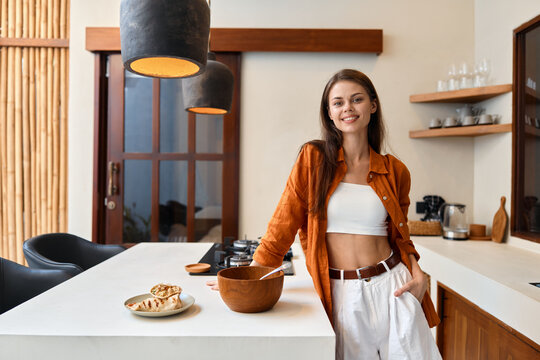 Young woman cooking in a stylish kitchen, wearing a casual outfit with a smile, representing healthy eating and modern lifestyle - Powered by Adobe