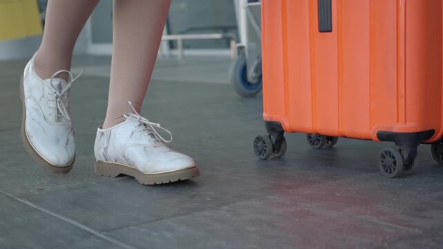A woman walks outside the airport wearing compression stockings and white shoes beside an orange suitcase, showing a close travel moment.