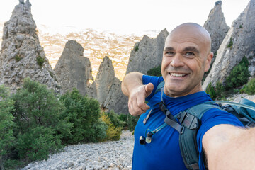 Hiker taking a selfie with thumbs up, outdoors.