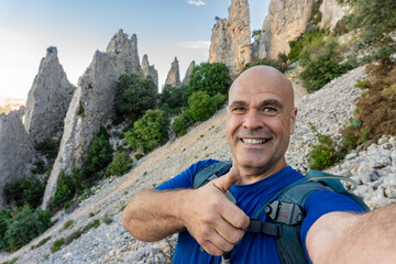 Hiker taking a selfie with thumbs up, outdoors.