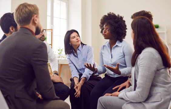 Afro American female coach leader talking holding briefing for team employees in office, explaining business strategy, plan, idea, people sitting at meeting with diverse colleagues for group therapy