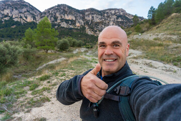 Hiker taking a selfie with thumbs up, outdoors.
