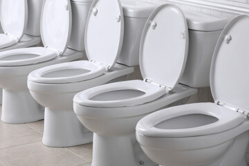 A clean, modern line of white porcelain toilets with open lids, set against a tiled floor and simple wall background, showcasing functional design.