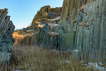 Majestic basalt columns in sunny landscape with snow and grasses