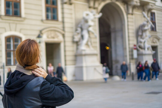 Woman from behind in black leather jacket gazing at historic Hofburg palace archway and statues in Vienna Austria concept of european travel, city breaks, tourism