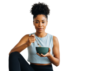 A serene young Black woman in athletic wear holds a green bowl, poised to eat. Her calm gaze and stylish workout attire suggest wellness, mindful eating, and balanced living—perfect for fitness, nutri