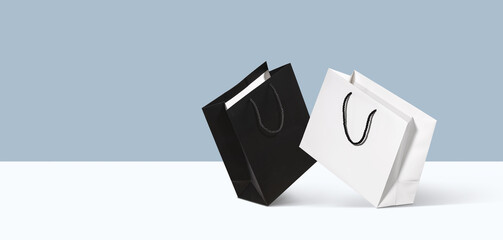 Two paper shopping bags, black and white on minimal blue duotone background. Concept of marketing design, seasonal discounts advertising layout and fashion shopping sale mockup. Banner, copy space
