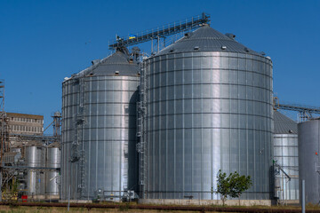 Metal silos stand tall against a clear blue sky at a modern agricultural facility in the early afternoon