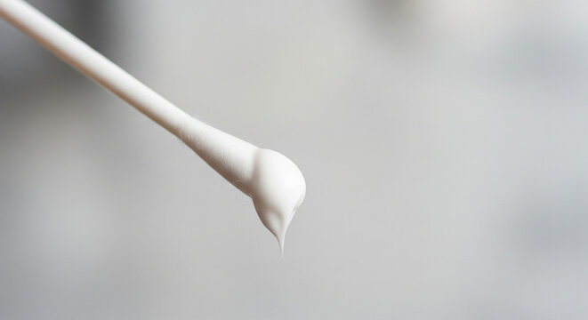 Macro Shot: Droplet of White Cream on a Cotton Swab Tip
An extreme close-up, macro shot captures a cotton swab (Q-tip) with a small, perfectly formed droplet of thick white or beige product