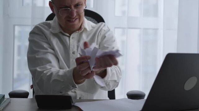 A man is experiencing a fit of anger and aggression at work.
A man tears up papers and scatters them around the office in anger.
A man working in a bright office is experiencing negative emotions.