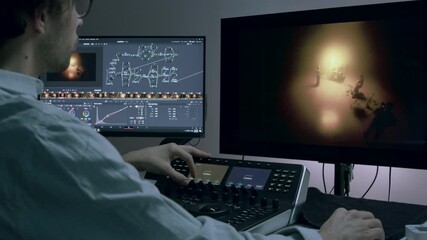 Color grading session in a modern editing suite, showcasing a male editor focused on adjusting visuals on dual monitors, emphasizing the intricate process of enhancing cinematic imagery