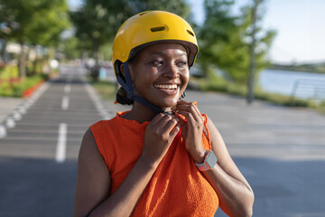 Cheerful African woman prepares to ride bicycle while adjusting yellow helmet