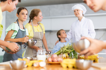 Children are excited to learn how to beat raw eggs with whisk under the guidance of a female chef