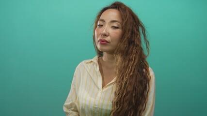 Woman looking sideways with long wavy hair and visible face in studio with teal backdrop; quiet contemplation.
