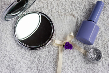 Self care essentials artfully arranged on a soft white towel. Featuring a compact mirror. Vibrant nail polish. Shimmering cosmetic glitter. And delicate decorative elements
