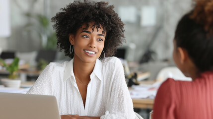 Black female employer interviewing Hispanic candidate, bright modern office, laptops and papers on table, positive professional vibe