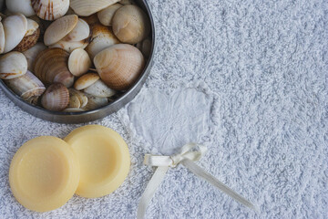 Natural spa elements on a soft towel, focusing on organic soaps, an assortment of seashells, and a decorative ribbon for a serene self care experience