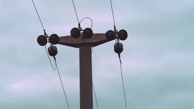 Concrete power pole with insulators and wires against a dull sky