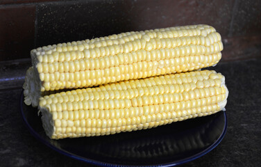 Raw corn on the cob on a dark plate. A delicious, ready-to-eat vegetable. A tasty and healthy dessert for both children and adults. A source of vitamins and fiber.