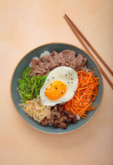 Traditional korean bibimbap with fried egg, beef and vegetables and other toppings top view on warm