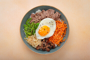 Traditional korean bibimbap with fried egg, beef and vegetables and other toppings top view on warm