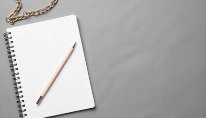 A blank notebook, a pen and a fragment of a silver chain on a gray surface - a symbol of a new turn in life