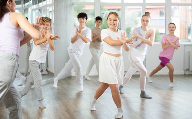 Obraz premium Young girls and boys repeat the movements of dance teacher, training in a spacious studio