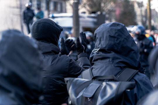 Anonymous masked left wing antifa, or so called black block is standing in front of a riot police line with helmets on in Germany to block other protesters.