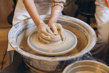 Child hands working clay on pottery wheel