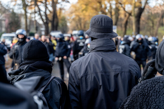 Anonymous masked left wing antifa, or so called black block is standing in front of a riot police line with helmets on in Germany to block other protesters.