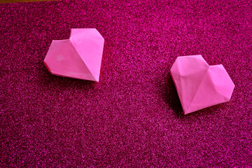 Two Pink Origami Paper Hearts on Sparkling Magenta Glitter Background. Handmade Folded Paper Hearts on Textured Pink Sparkle Backdrop for Valentine's Day