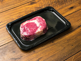 Premium top quality beef rib eye steak in black plastic vacuum packed package on wooden table. Thick high value meat with lots of marbling for great taste and flavor.
